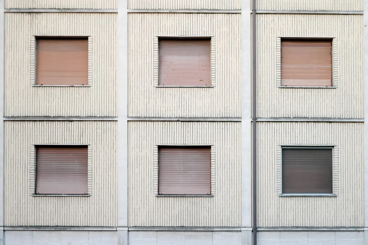 Façade d'immeuble en panneaux de béton striés, six fenêtres carrées aux volets roulants baissés saumon et gris